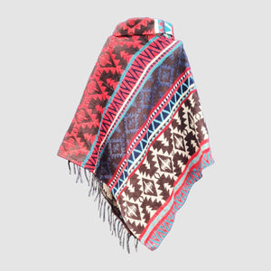 Colorful black and red patterned poncho with fringes on a light gray background