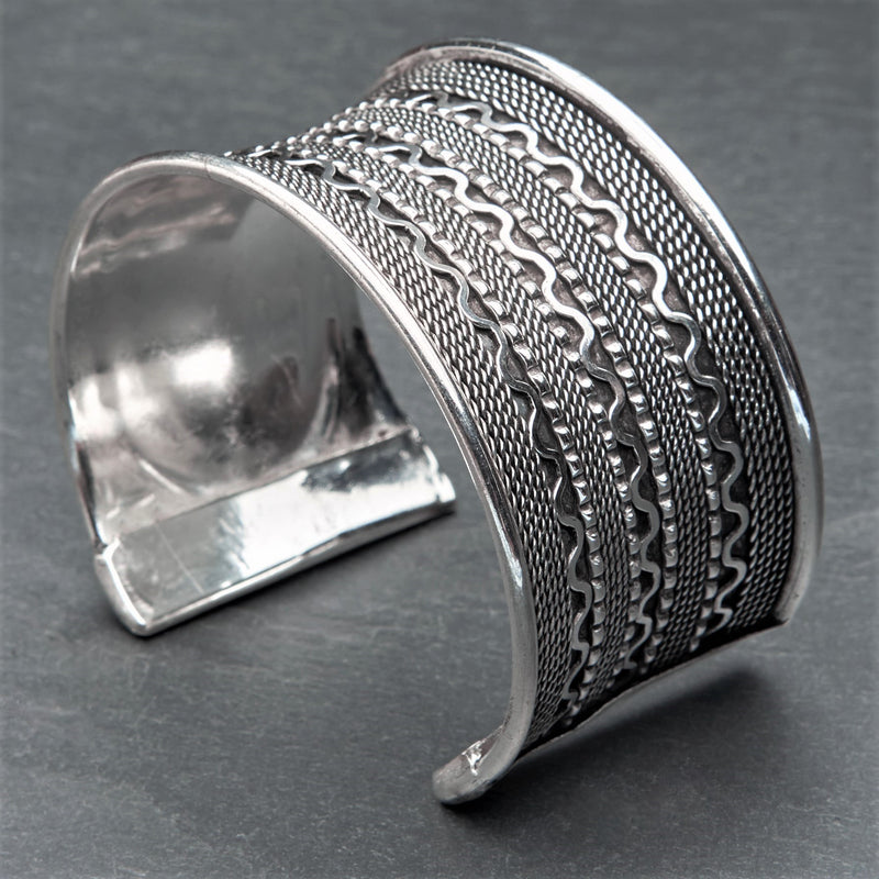 An adjustable, wide concave shaped silver wavy patterned cuff bracelet designed by OMishka.