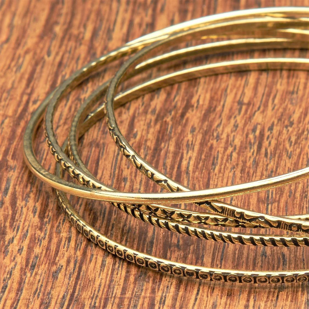 A handmade, pure brass set of 5 thin bangle bracelets each etched with traditional Indian patterns designed by OMishka.